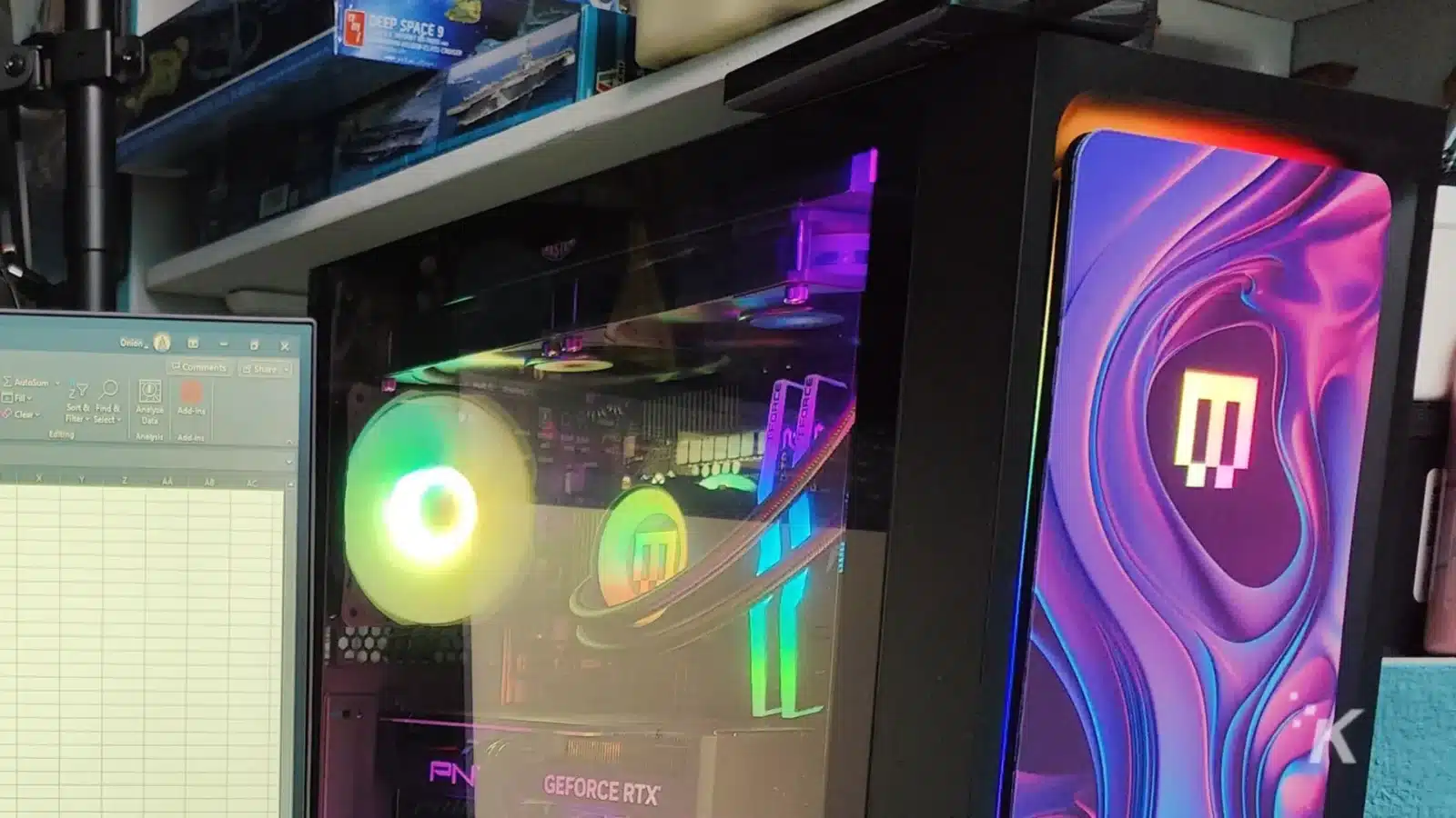 evaluating the excel-lent maingear mg-1 platinum A desktop pc with rgb lighting visible through a clear side panel, featuring a geforce rtx graphics card, beside a monitor with colorful wallpaper.