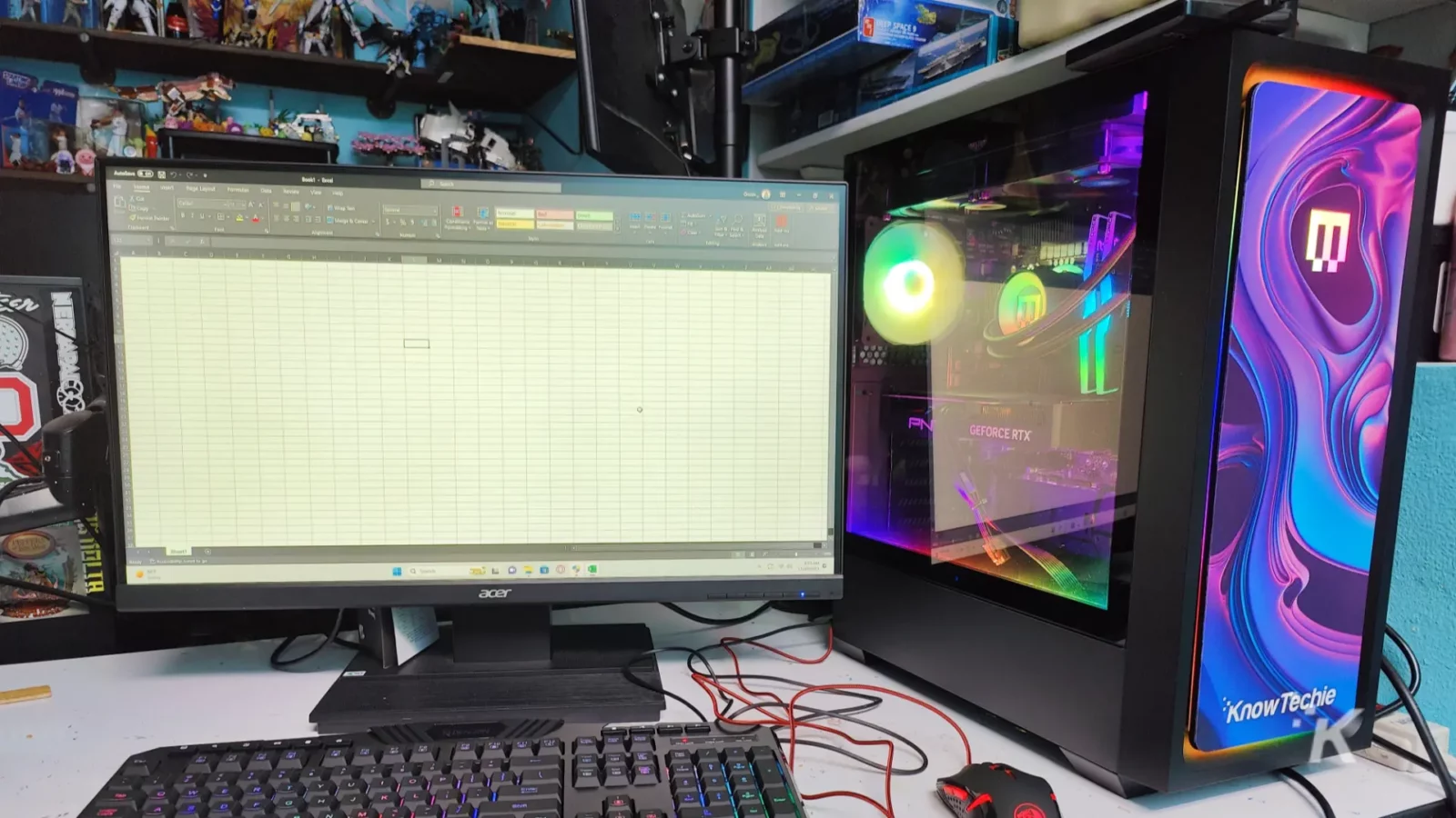 evaluating the excel-lent maingear mg-1 platinum The image shows a desk with a computer monitor displaying a spreadsheet, a backlit keyboard, a custom pc with rgb lighting, and various collectibles on shelves.