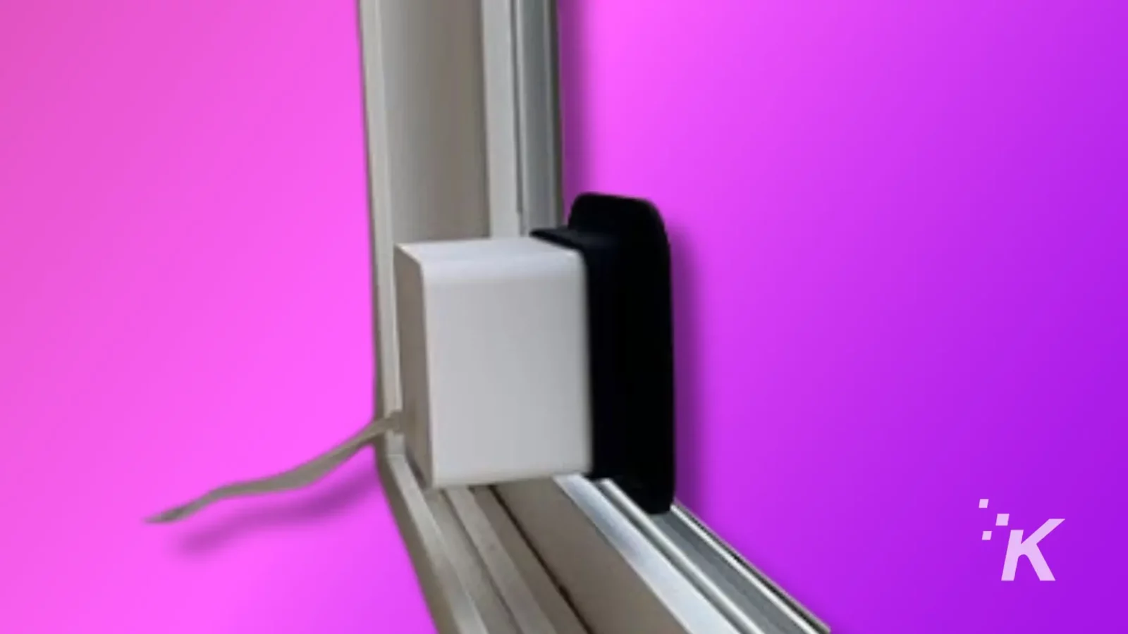 top 5 places to hide a wyze camera on your property A device with a white body and black top is mounted on a window frame against a vibrant pink background with a kiwico logo in the corner.