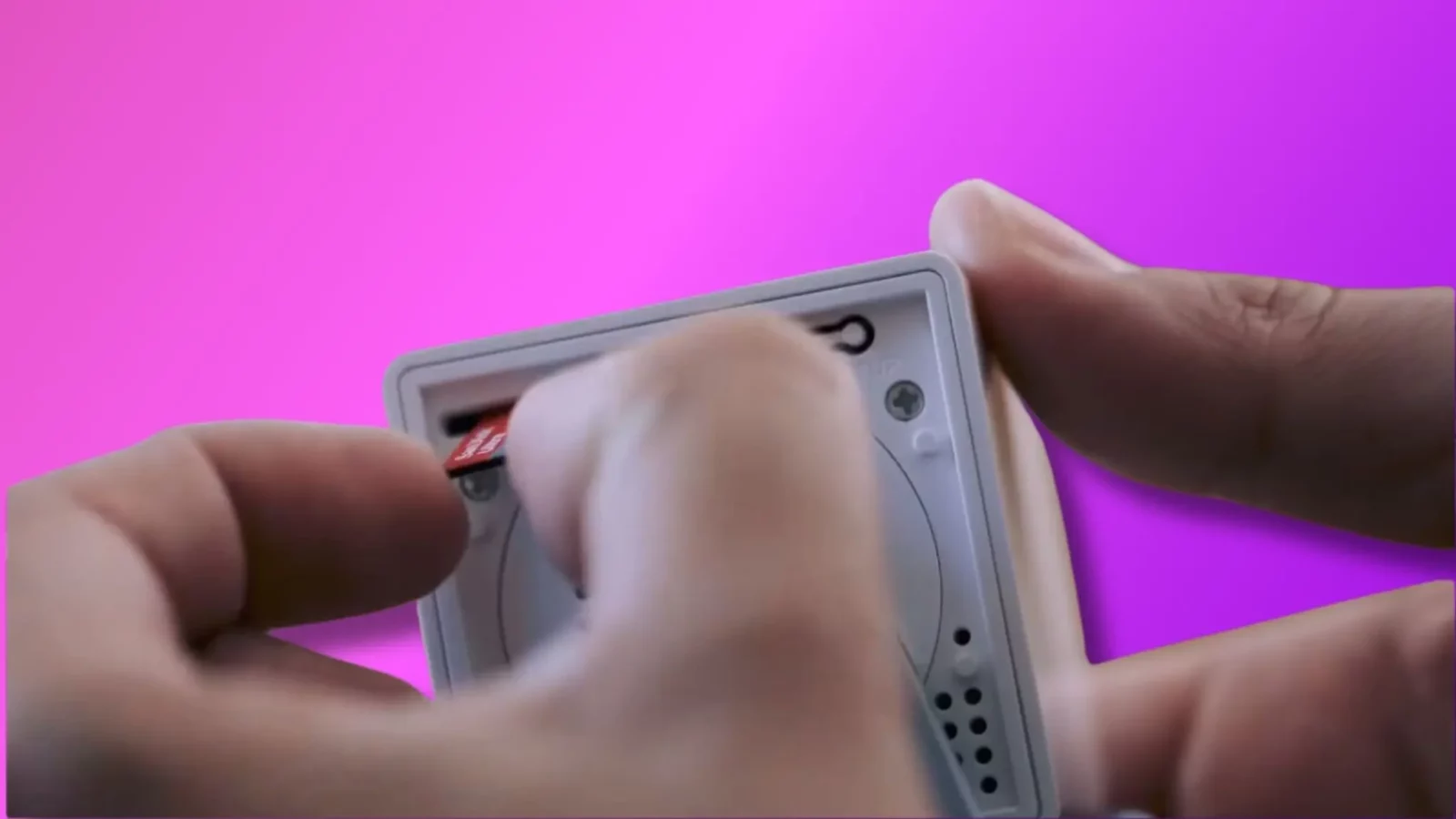 how to fix a wyze cam not recording to its microsd card A person is inserting a red sd card into a gray handheld device against a vibrant pink background. Their fingers are in focus, pressing the card in.